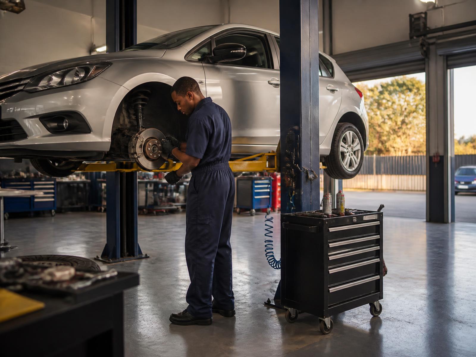 Mechanic inspecting the front brakes of a car raised on a hoist in a South African workshop